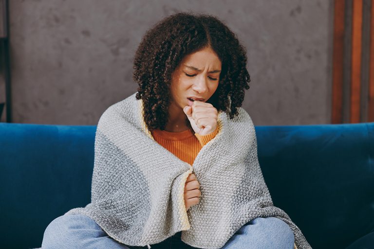A teen wrapped in a blanket coughing into her fist.